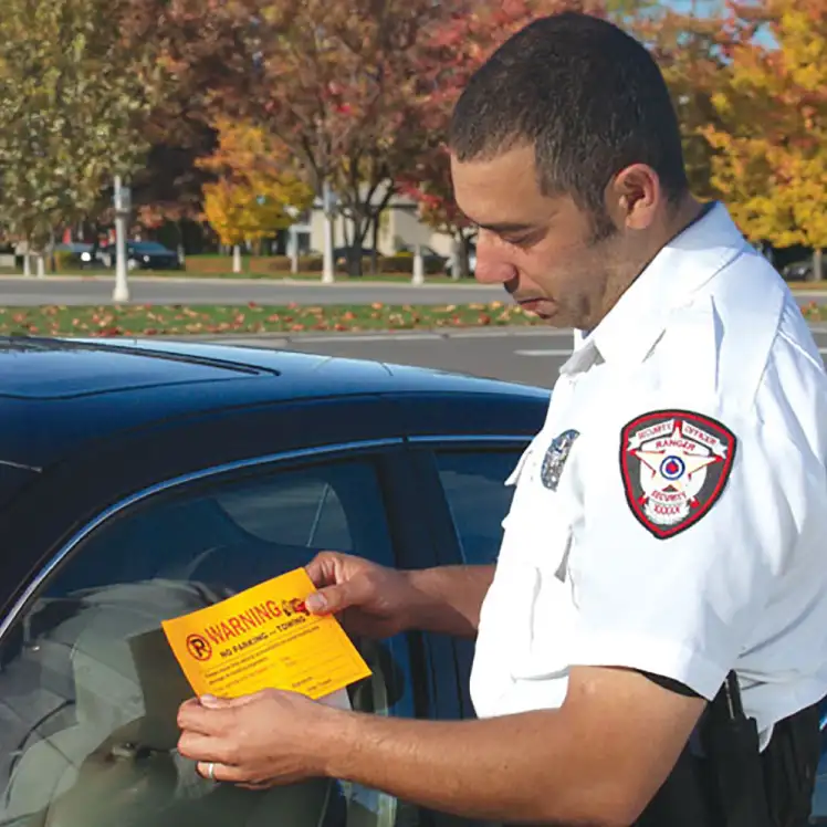 Fluorescent orange Parking Violation Sticker Warning No Parking being applied to illegally parked vehicle.