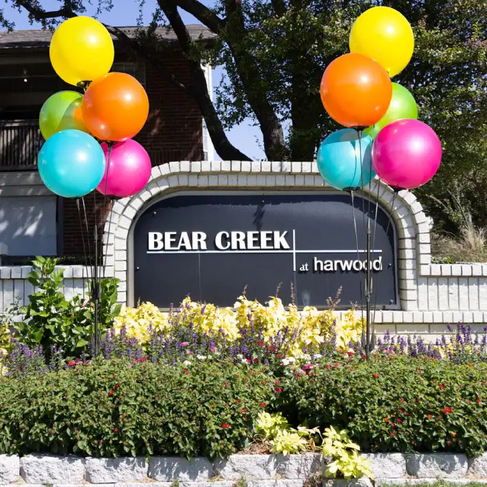 Two colorful reusable balloon clusters mounted in-ground next to an apartment sign.
